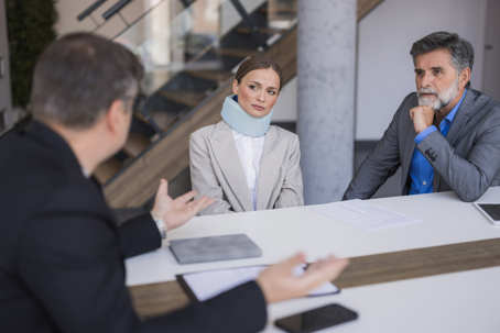 Woman with neck brace discussing legal compensation with her lawyer and family member